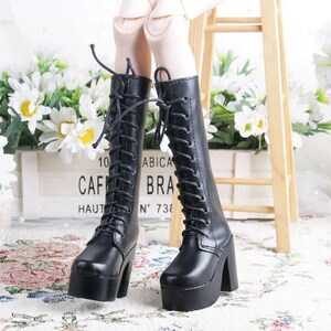 May include: Black, lace-up platform boots with thick heels. The boots have a rounded toe and are made of a smooth material. The boots are part of a doll's outfit. The background includes white flowers and a wooden sign.