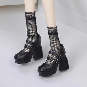 May include: A pair of black platform Mary Jane shoes with double buckled straps and thick block heels, worn with black fishnet socks featuring a delicate lace trim at the top. The shoes have a rounded toe and a smooth, matte finish.