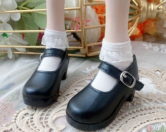 May include: A pair of black Mary Jane style shoes with a buckle closure. The shoes have a small heel and are worn with white socks trimmed with lace. The shoes are approximately 2 inches in height.