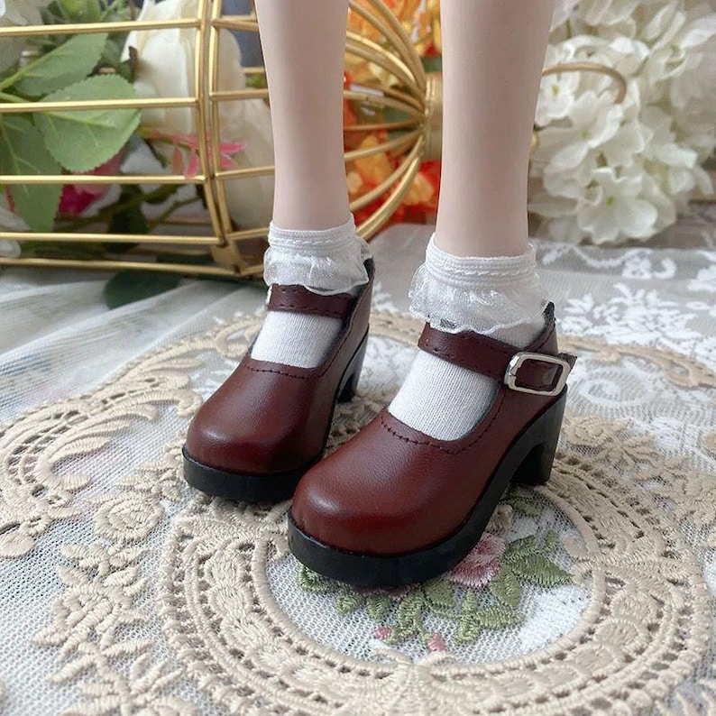 Pu&ograve; includere: Scarpe Mary Jane in pelle marrone con cinturino e fibbia. Le scarpe hanno una suola platform nera e sono indossate con calzini bianchi con finiture in pizzo. Stile classico.