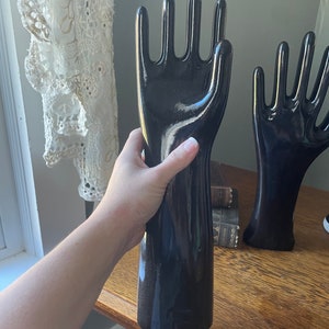 May include: Two black ceramic mannequin hands with long, slender fingers. The hands are posed with the palms facing outward. The hands are glossy and have a smooth finish.