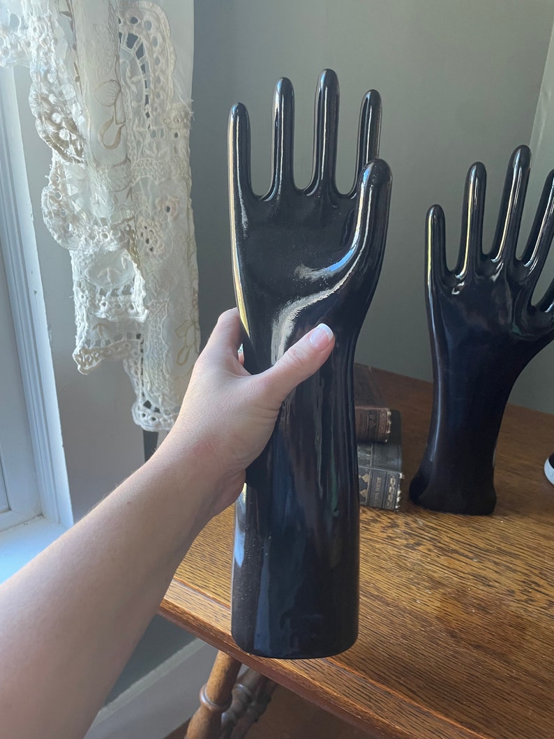 May include: Two black ceramic mannequin hands with long, slender fingers. The hands are posed with the palms facing outward. The hands are glossy and have a smooth finish.