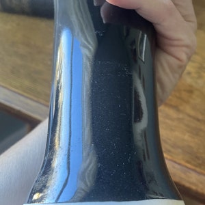 May include: Black ceramic vase with a white base. The vase has a glossy finish and is shaped like a tall, slender bottle.