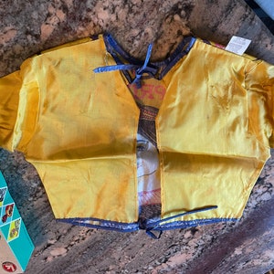 May include: A yellow satin costume top with a blue trim and a tie at the neck. The top has a printed design of a woman's face and a floral pattern.