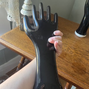 May include: A black ceramic hand sculpture with a glossy finish. The hand is posed with fingers extended and the palm facing outward. The sculpture is approximately 12 inches tall.