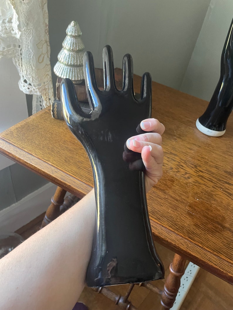 May include: A black ceramic hand sculpture with a glossy finish. The hand is posed with fingers extended and the palm facing outward. The sculpture is approximately 12 inches tall.