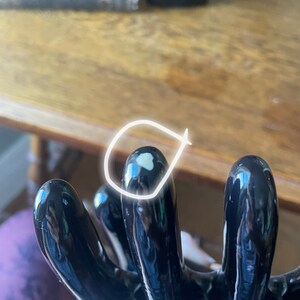 May include: Black ceramic hand-shaped vase with five fingers. The vase has a glossy finish and a white spot on one of the fingers.
