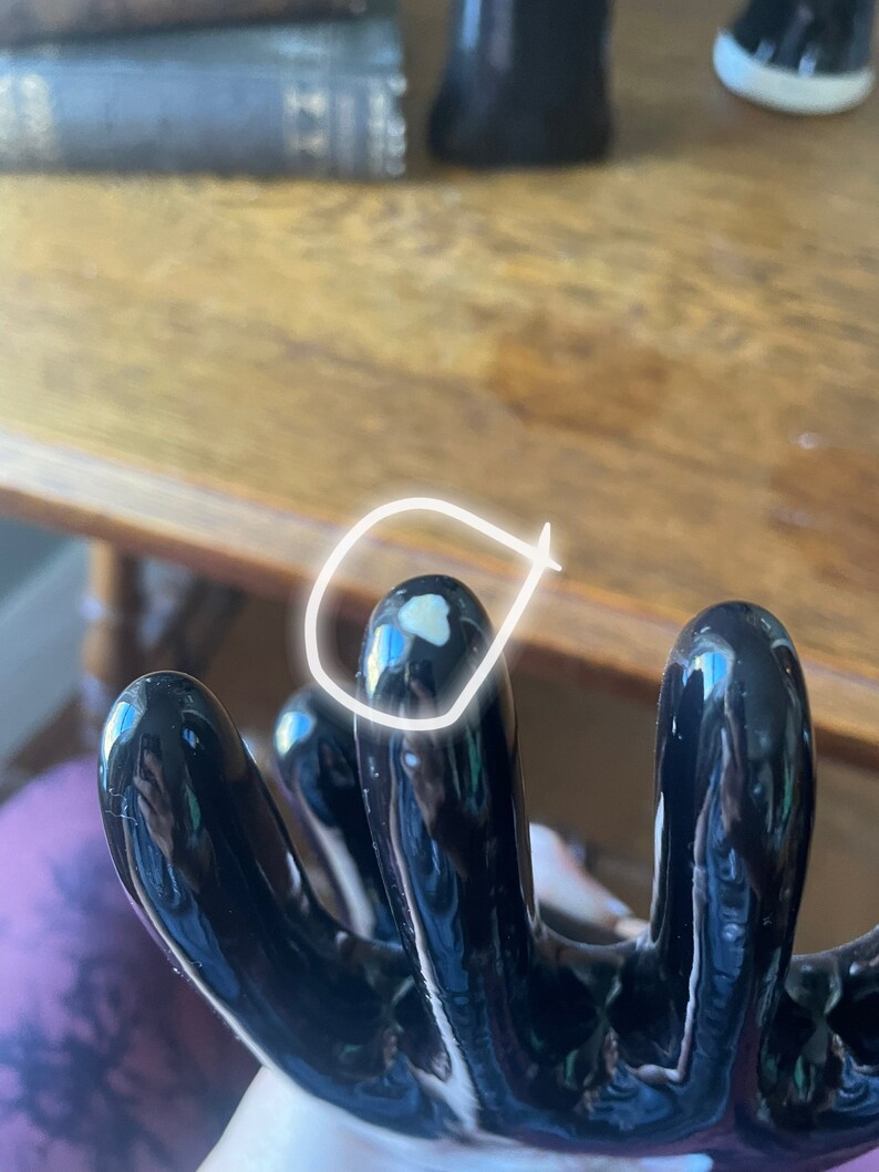 May include: Black ceramic hand-shaped vase with five fingers. The vase has a glossy finish and a white spot on one of the fingers.