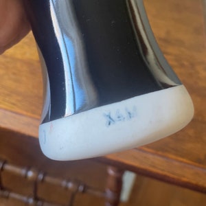 May include: Black ceramic vase with a white base. The base has the text "X.A.M." written in blue ink.