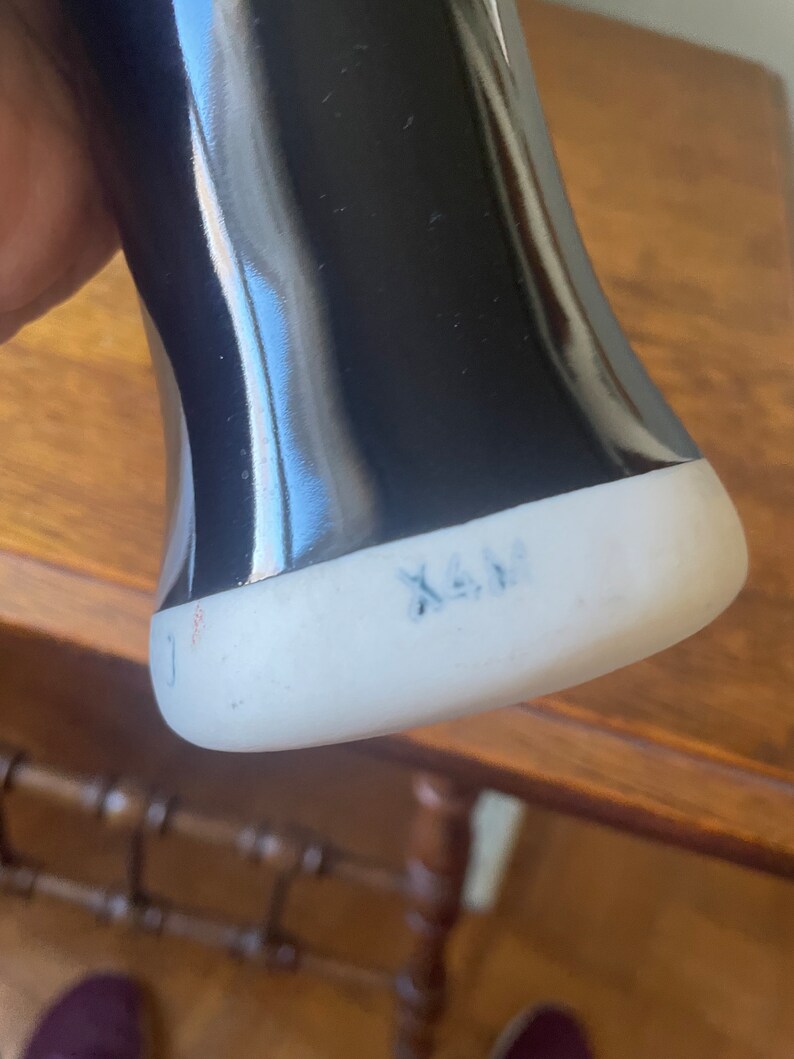 May include: Black ceramic vase with a white base. The base has the text "X.A.M." written in blue ink.