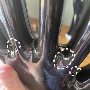 May include: Black ceramic hand sculpture with five fingers. The fingers are long and slender, and the hand is slightly curved. The sculpture is glossy and has a smooth finish.
