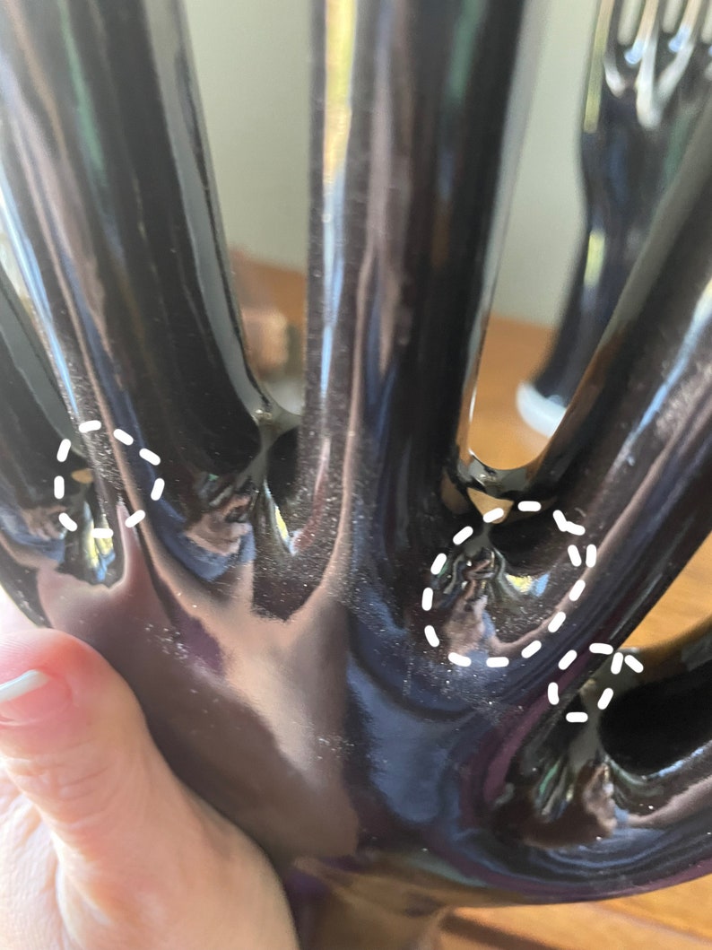 May include: Black ceramic hand sculpture with five fingers. The fingers are long and slender, and the hand is slightly curved. The sculpture is glossy and has a smooth finish.