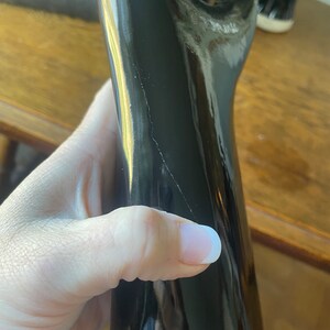 May include: A black, glossy, wooden walking stick with a slight crack in the finish.