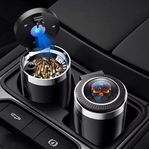 May include: Black car ashtray with a skull design. The ashtray is cylindrical with a stainless steel rim and a lid that opens to reveal a blue light. The second ashtray has a skull design on the lid.