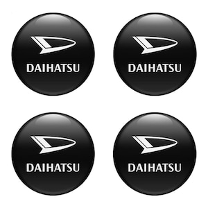 May include: Four black, circular Daihatsu emblems. Each emblem features the Daihatsu logo in white, a stylized arrow shape above the brand name. The emblems have a glossy finish.