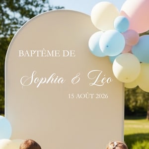 Puede incluir: Un arco crema con el texto "BAPTÊME DE Sophia & Léo 15 AOÛT 2026" está decorado con globos pastel. Niños jugando en la hierba frente al arco. La escena se desarrolla al aire libre en un día soleado.