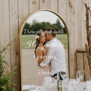 Może przedstawiać: Złote lustro w kształcie łuku odbijające parę. Lustro zawiera francuski tekst: "Votre plan de table", "30+ polices", "Couleurs", i "au choix". Tło to drewniana ściana.
