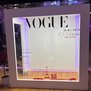 Peut inclure: Un photomaton encadré de blanc avec le mot "VOGUE" en grandes lettres noires. La date "21.05.2024" et le texte "White Circus Emily in Paris" sont également visibles. Une silhouette de la Tour Eiffel et d'autres bâtiments se trouve en bas.