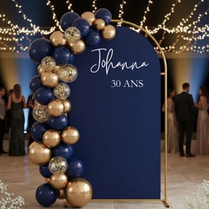 Puede incluir: Un soporte de fondo arqueado azul marino con marco de metal dorado, decorado con una guirnalda de globos azul marino, oro metálico y globos transparentes con confeti. El centro presenta el texto blanco Johanna y 30 ANS en fuente script y serif.