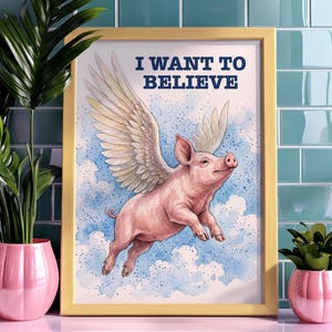 May include: A framed print showing a pink pig with feathered wings, flying in a blue sky with clouds. The text "I WANT TO BELIEVE" is in navy blue. The frame is a light yellow colour.