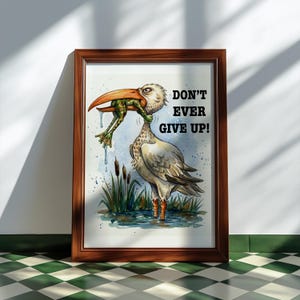 May include: Framed watercolor print featuring a bird with a frog in its beak, set in a marsh scene. The bird is depicted with detailed feathers and an orange beak. The text "DON'T EVER GIVE UP!" is displayed in black.