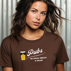May include: Dark chocolate brown t-shirt with the word "Pubs" in white script, featuring a graphic of a beer glass with sunglasses. The text "THE OFFICIAL SUNBLOCK OF IRELAND" is below the word "Pubs".