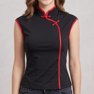 May include: A sleeveless black top featuring a mandarin collar and a diagonal front closure accented with bright red piping. The garment includes a small decorative knot fastener at the neckline and red trim along the armholes and side seam.