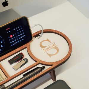 May include: A wooden desk organizer with multiple compartments. It features a charging station for a phone displaying a June calendar, a USB drive, and a pen. The organizer has a personalized section with the name "Samuel" engraved on it.