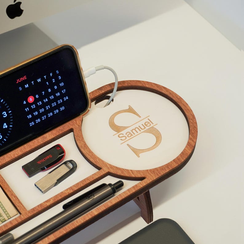 May include: A wooden desk organizer with multiple compartments. It features a charging station for a phone displaying a June calendar, a USB drive, and a pen. The organizer has a personalized section with the name "Samuel" engraved on it.