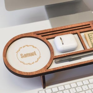 May include: A wooden desk organizer with multiple compartments. It features a round section with the name "Samuel" and a decorative wreath. Other compartments hold a white case, a pen, and a ten-dollar bill.