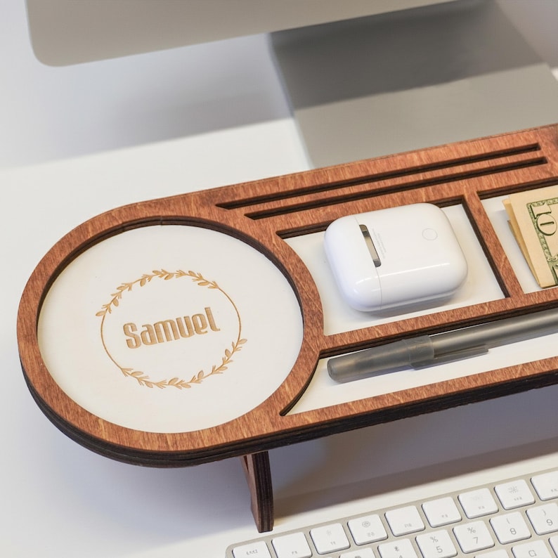 May include: A wooden desk organizer with multiple compartments. It features a round section with the name "Samuel" and a decorative wreath. Other compartments hold a white case, a pen, and a ten-dollar bill.