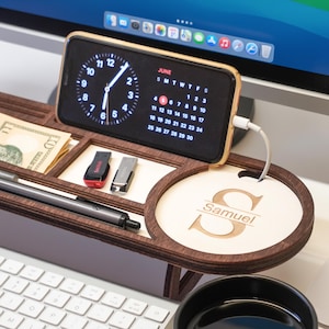 May include: A wooden desk organizer with a phone charging, a pen, cash, and USB drives. The phone displays a clock and calendar. The organizer has a personalized round section with the name "Samuel".
