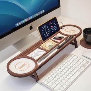 May include: A wooden desk organizer with multiple compartments, holding a smartphone, money, pens, and earbuds. The organizer has a dark brown finish with white accents and a personalized circular design. A computer keyboard and monitor are in the background.