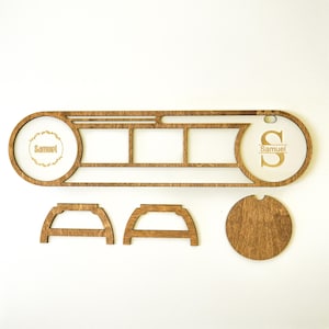 May include: A wooden personalized photo display with the name "Samuel" engraved on two circular sections. The display includes spaces for photos and additional wooden components. The design is made of light brown wood.