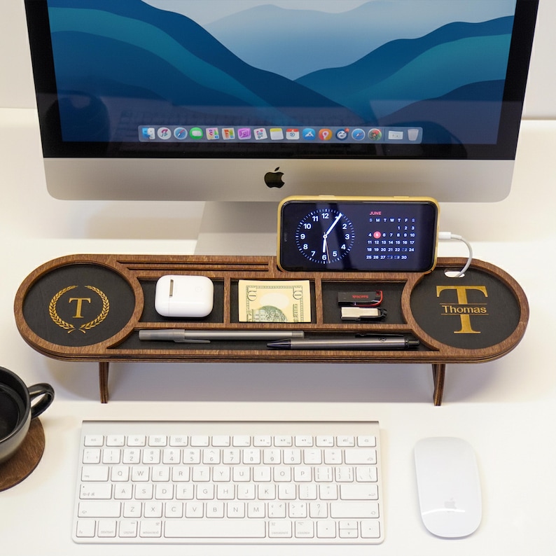 May include: A wooden desk organizer with a phone charging station, two round trays with the letter "T" and the name "Thomas", and compartments for pens, money, and other small items. A phone displays the time and date.