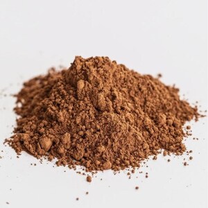 Puede incluir: Un mont&oacute;n de polvo fino y marr&oacute;n sobre un fondo blanco. El polvo tiene una apariencia texturizada y granulada, con variaciones de tono y sombra. El color general es un marr&oacute;n rico y terroso.