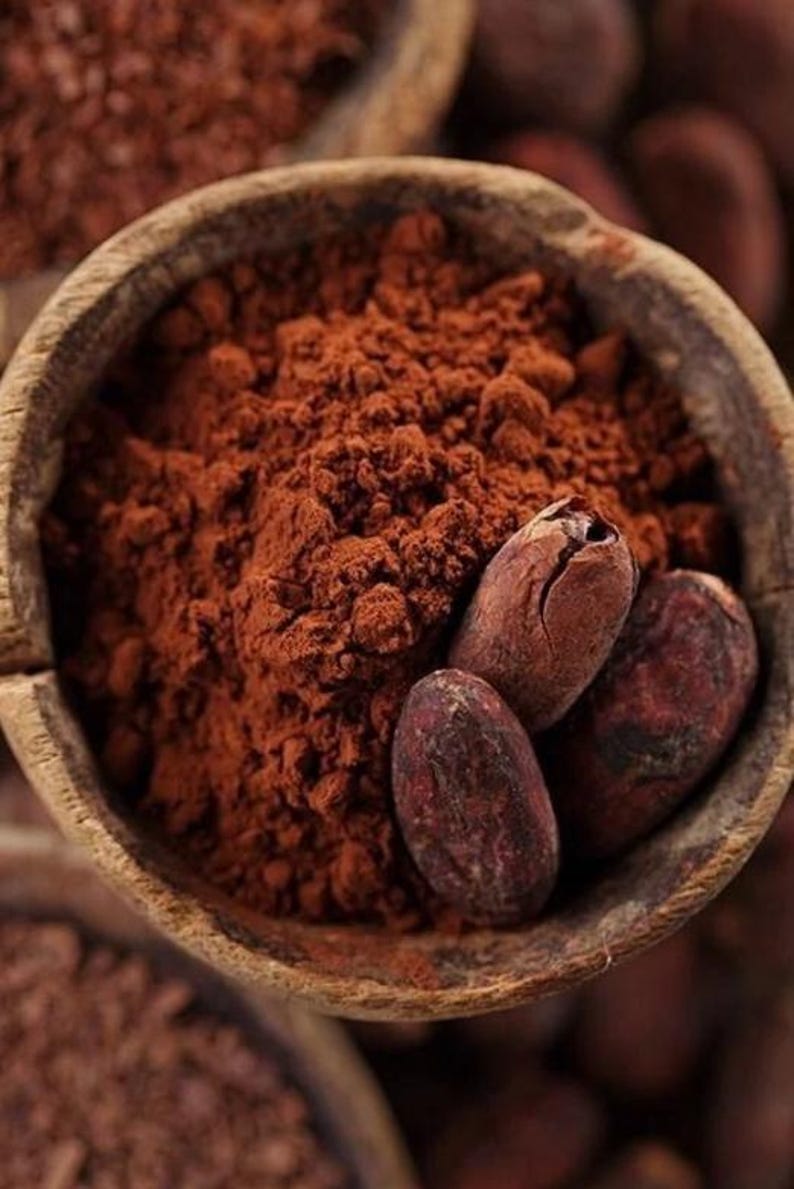 Puede incluir: Primer plano de un cuenco de madera lleno de cacao en polvo marr&oacute;n oscuro y varios granos de cacao. El polvo tiene una textura fina y los granos son de color marr&oacute;n oscuro con una superficie texturizada. La imagen destaca los ingredientes del chocolate.