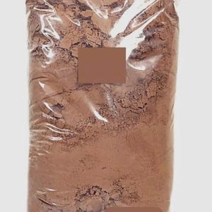 Puede incluir: Una bolsa grande de pl&aacute;stico transparente llena de un polvo fino de color marr&oacute;n. La bolsa est&aacute; sellada y tiene una etiqueta rectangular marr&oacute;n. El polvo parece ser un ingrediente a granel, posiblemente para hornear u otros usos culinarios.