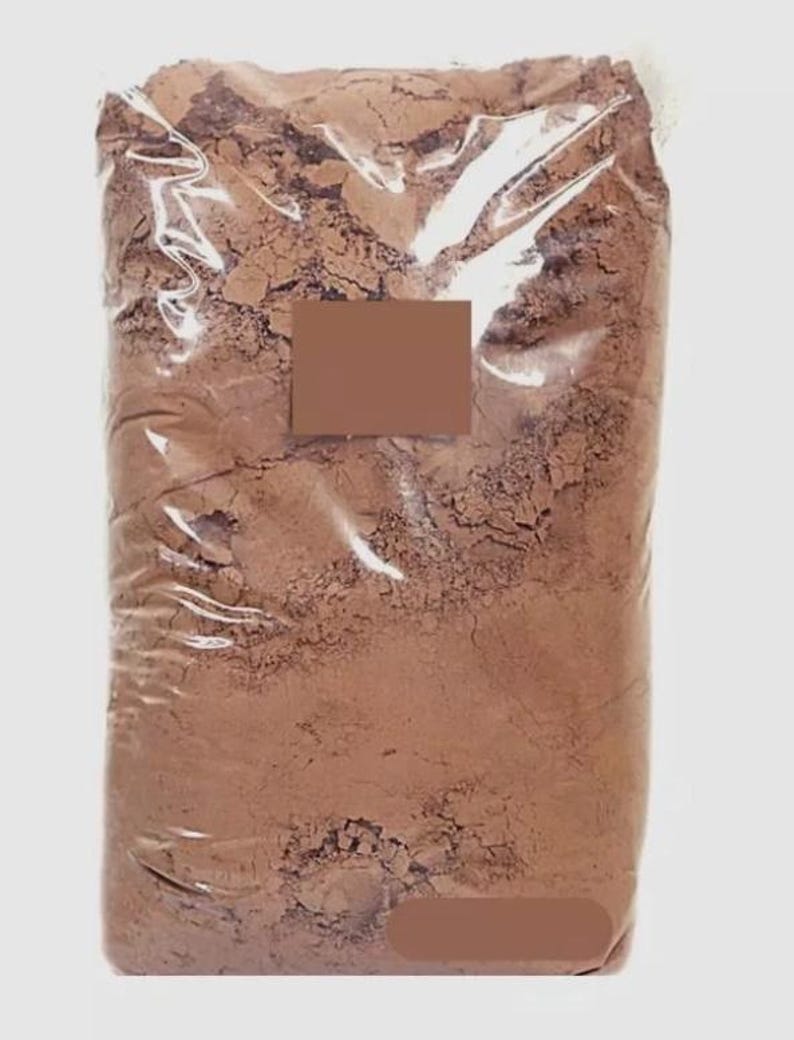 Puede incluir: Una bolsa grande de pl&aacute;stico transparente llena de un polvo fino de color marr&oacute;n. La bolsa est&aacute; sellada y tiene una etiqueta rectangular marr&oacute;n. El polvo parece ser un ingrediente a granel, posiblemente para hornear u otros usos culinarios.