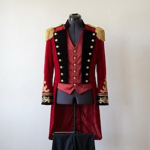 May include: A red velvet tailcoat featuring black lapels, gold-tone buttons, and gold fringe epaulets. The cuffs are adorned with gold embroidery. Underneath is a red vest with a button-down front, displayed on a mannequin torso.