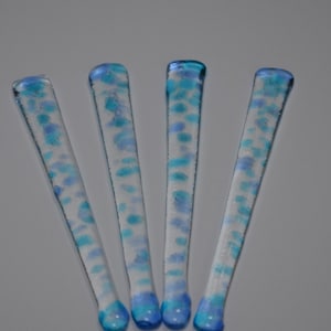 May include: Four glass stirring sticks with a blue and white speckled design. The sticks are clear glass with blue and white flecks throughout. The ends of the sticks are rounded.