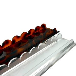 May include: Three decorative trays with scalloped edges. One is clear, one is a tortoiseshell pattern, and the other is a dark brown color. The trays are made of a transparent material and are angled towards the viewer.