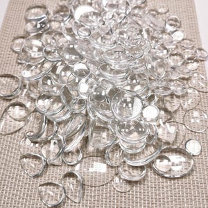Peut inclure: Un ensemble de pierres décoratives en verre transparent de différentes formes, rondes, ovales et en forme de goutte. Les pierres sont disposées sur une surface texturée de couleur neutre, créant un effet scintillant. Idéal pour l'artisanat et la décoration intérieure.