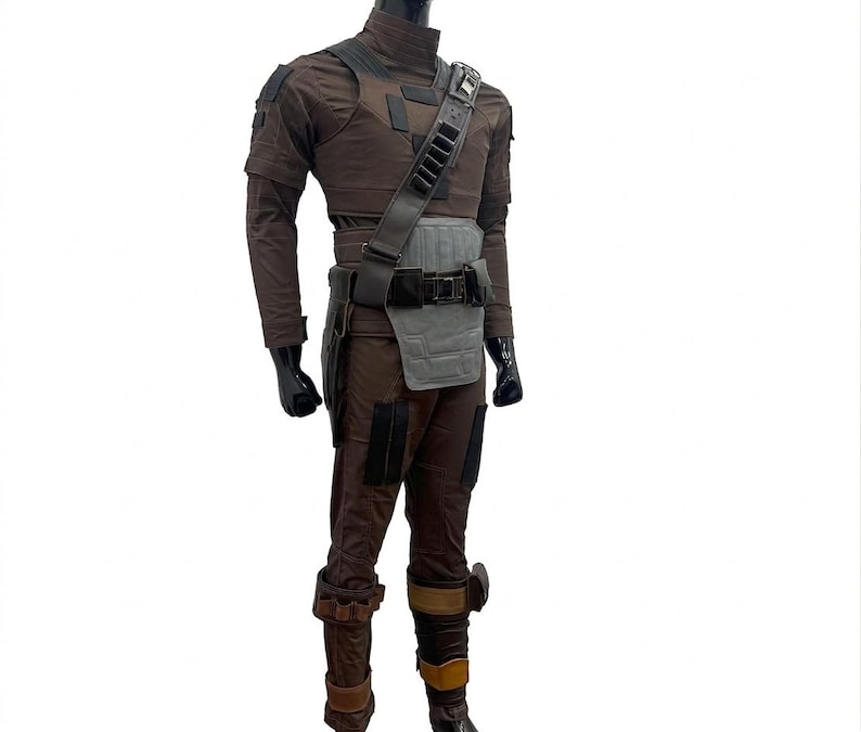 K&ouml;nnte beinhalten: Ein braunes und graues Kost&uuml;m mit hohem Kragen, Schulterpolstern und einem Werkzeugg&uuml;rtel. Das Kost&uuml;m umfasst eine passende Hose und Stiefel mit schwarzen Handschuhen. Das Outfit ist mit mehreren Taschen und Riemen versehen.