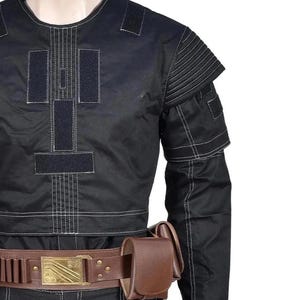 May include: A black long-sleeve tactical shirt with white contrast stitching, featuring rectangular hook-and-loop panels on the chest and ribbed shoulder detailing. A brown leather utility belt with a gold-toned buckle and pouch is worn.