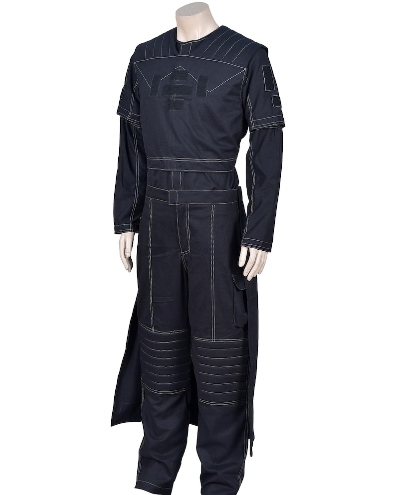 May include: A dark navy blue jumpsuit with white stitching. The long-sleeved top has a logo, and the trousers have cargo pockets and knee padding. The outfit includes a long, split panel on the side.