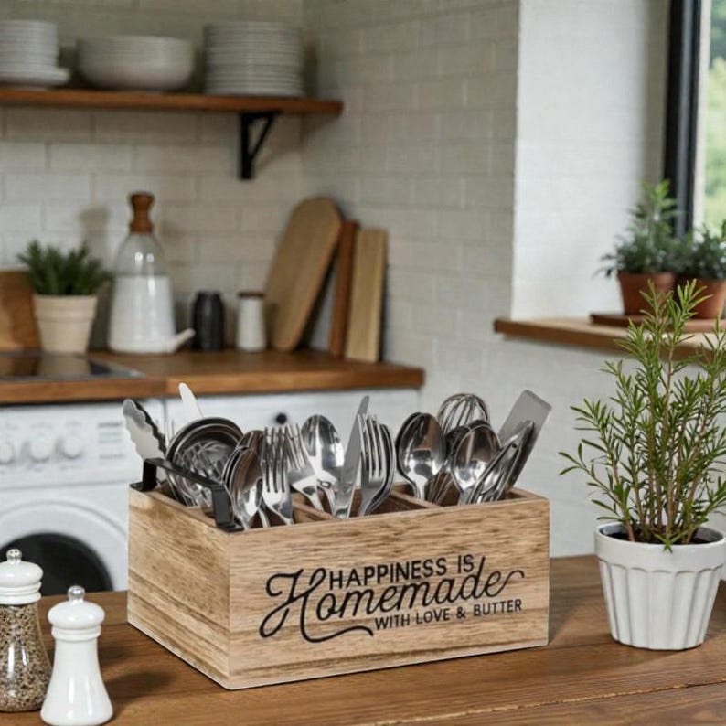 K&ouml;nnte beinhalten: Ein h&ouml;lzerner Besteckhalter mit dem Text "Happiness is Homemade with Love & Butter" enth&auml;lt verschiedene Bestecke. Der Halter steht auf einer Holzoberfl&auml;che, mit einer kleinen Topfpflanze und Salz- und Pfefferstreuern im Vordergrund.