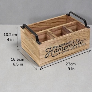 K&ouml;nnte beinhalten: Rechteckiger Holz-Organizer mit vier F&auml;chern und schwarzen Metallgriffen. Auf der Vorderseite steht der Text "HAPPINESS IS Homemade WITH LOVE & BUTTER". Er ist 23 cm lang, 16,5 cm breit und 10,2 cm hoch.