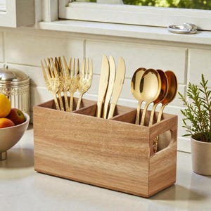 Puede incluir: Un organizador de cubiertos de madera con tres compartimentos, que contiene tenedores, cuchillos y cucharas doradas. Los utensilios tienen mangos decorativos. El organizador tiene un asa lateral y está sobre una encimera blanca.