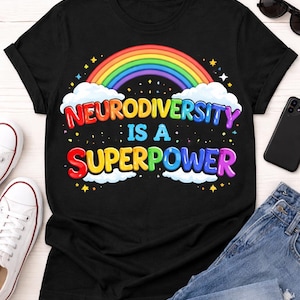 Peut inclure: T-shirt noir avec un arc-en-ciel et l'inscription colorée "Neurodiversité est un Superpouvoir". Il est présenté avec un jean bleu, des baskets blanches, des lunettes de soleil et un smartphone.
